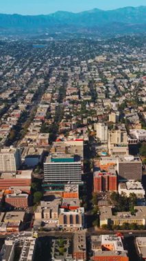 Güneşli bir günde yoğun mimarisi olan güzel güneşli Los Angeles. Arkaplanda dağlar. Hava görüntüsü. Dikey video