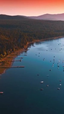 Gün batımında görkemli Tahoe Gölü kıyısında. Suda yüzen çok sayıda tekne var. Pembe gökyüzü ve arka planda dağlar. Dikey video