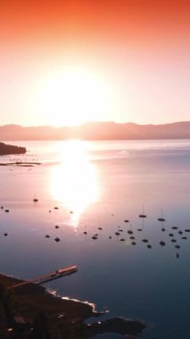 Tahoe Gölü 'nün çok sayıda teknesi olan muhteşem manzarası. Orman kıyısı ve güneş suyun pürüzsüz yüzeyine yansıyor. Arkaplanda pembe gökyüzü. Dikey video