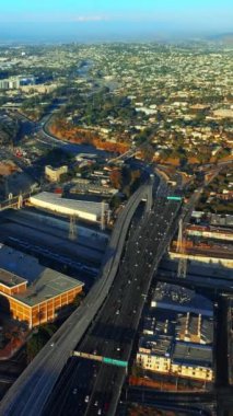 Gündüz vakti Los Angeles otoyollarında hareketli bir trafik var. Şehrin güneşli manzarası dağların arka planında. Üst Manzara. Dikey video