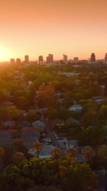 Güneşin batışı güzel Sacramento, California, ABD üzerinde. İHA, turuncu gökyüzünün arka planında yeşil rahat şehrin üzerinde uçuyor. Dikey video