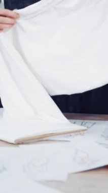 İki terzi masaya yeni bir bez seriyor. Atölyedeki profesyonel terzilerin ellerinde beyaz ve kırmızı kumaş. Terziler atölyede elbise dikmek için malzeme hazırlıyorlar..