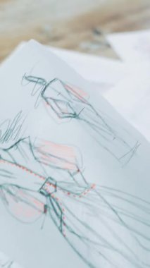 Moda tasarımcısı farklı çizimlere bakıyor ve uygunsuz olanı atıyor. Bir terzinin işyeri. Masanın üzerine yazılmış bir sürü modern elbise çizimi var..