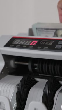 Adam para sayma ekipmanına bir tomar dolar harcıyor. Banknotlar ve Benjamin Franklin portresi makineyi teslim ediyor. Kapatın. Dikey video