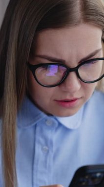 Endişeli, uzun saçlı bir kadın iki elinde tuttuğu telefona bakıyor. Akıllı telefondan haber okuyan endişeli bayan. Dikey video