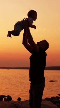 Gülümseyen baba küçük oğlunu havaya fırlatıyor. Baba ve oğul doğada ailecek vakit geçiriyorlar. Gün batımında arka planda nehir. Dikey video