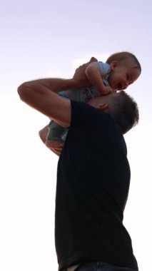 Önemseyen baba oğlunu havaya kaldırıyor ve küçük göbeğini öpüyor. Babacığın bebeğini fırlatıp atıyor. Düşük açı. Dikey video