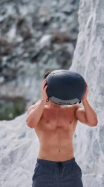 Adam dışarıda sağlık topu egzersizi yapıyor. İlaç topuyla egzersiz yapan sağlıklı genç adam. Dikey video.