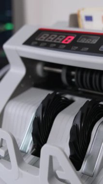 50 Euro 'luk banknotları olan para sayma makinesi. Kapatın. Laptop arka planda bulanık olarak açıldı. Dikey video