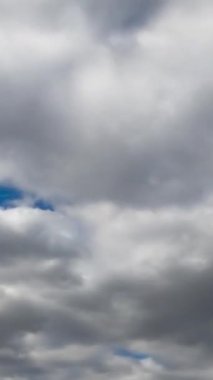 Mavi gökyüzünü tamamen kaplayan gri bulutlar. Düşük açı. Zaman ayarlı. Dikey video