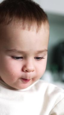 Sevimli erkek bebek yavaşça yemek çiğniyor. Sevimli çocuk peynir parçalarını bir yerden başka bir yere koyuyor. Kapatın. Dikey video