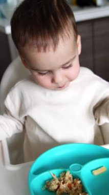 Küçük bir çocuk için yemek vakti geldi. Şirin bebek tabağını yakına çekiyor. Kapatın. Üst Manzara. Dikey video