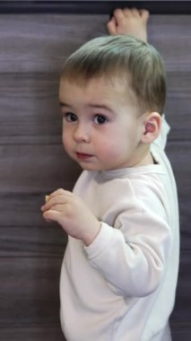 Beyaz kazaklı, melek gibi çocuk mutfak büfesinde duruyor. Gülümseyen çocuk aynı anda hem bir şeyler yiyip hem de kapıları açıyor. Bebek odadan çıkar ve uzaklaşır. Dikey video