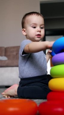 Tatlı çocuk piramit halkalarını yerden alıyor. Yürüyen çocuk piramit inşa eder ve boyut ve renkleri öğrenir. Düşük açı. Dikey video