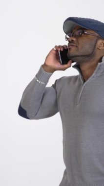 Zenci adam telefonla konuşuyor. Gri kazaklı ve şık şapkalı Afro-Amerikan bir adam beyaz stüdyo geçmişiyle ilgili bir iş konuşmasını yönetiyor. Ağır çekim. Dikey video
