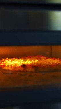Sıcak fırında lezzetli pizza. Şef özel pizza spatulasıyla fırını hazırlıyor. Pizzacıda pizza pişirme işlemi. Dikey video