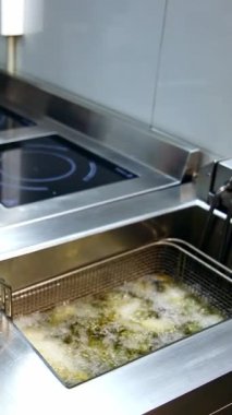 Restoranın mutfağında yemek pişirmek. Fırının arka planında kızartma kızartması ve kızartma kızartması. Kızartma makinesinde kızarmış patates. Dikey video