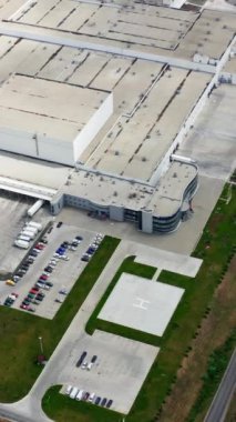 Yeşil alanda endüstri. Modern fabrikanın yakınında kamyonlar ve arabalar. Otoparkı olan büyük bir sanayi fabrikasının çatıları. Hava görüntüsü. Dikey video