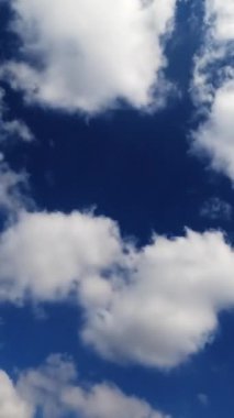 Gökyüzünde hızla süzülen beyaz pamuk bulutları. Güzel bulutlu mavi yaz gökyüzü. Zaman aşımı. Dikey video