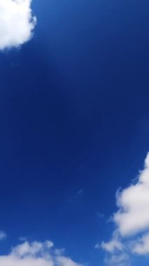 Açık beyaz bulutlar parlak mavi gökyüzünde hızla süzülüyor. Yumuşak bulutlar yaz güneşinin ışınlarını yansıtıyor. Dikey video