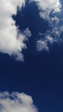 Gökyüzünde kabarık beyaz bulutlar oluşuyor. Yaz mevsiminin hızlı hareket süresi. Güzel bulutlarla dolu parlak gökyüzü arkaplanı. Dikey video