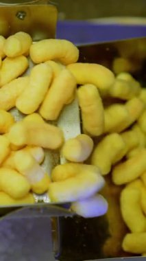 Taşıyıcı banttaki metal kutular tatlı atıştırmalıklarla dolduruluyor. Modern gıda fabrikasında mısır gevreği üretimi. Kapatın. Dikey video