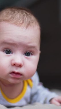 Güzel, beyaz bir çocuk karnının üstünde başı yukarıda yatıyor. Meraklı küçük çocuk yana bakıyor, gözleri açık. Kapatın. Dikey video