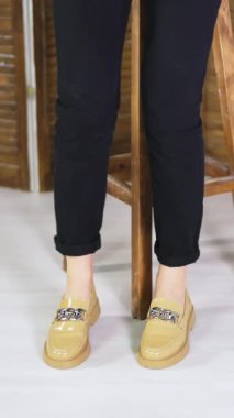 Siyah kotlu kadın yeni ayakkabılarını göstermek için tahta bir tabureden kalkar. Zincir süslemeli bej renkli modadan ayakkabılar. Dikey video