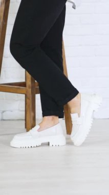 Modaya uygun beyaz ayakkabı sunumu. Kadın model, ahşap tabutun yanında şık ayakkabılar giyer, ileri geri yürür. Dikey video