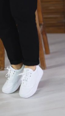 Rahat beyaz ayakkabıların içine atlayan bir model. Bir kadın spor ayakkabılarını göstermek için döner ve zıplar. Dikey video