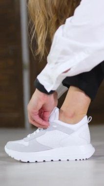 Bayan beyaz spor ayakkabıları gösteriyor. Kadın rahat ayakkabılara dokunmak için çömelmiş. Kapatın. Arkaplan bulanık. Dikey video