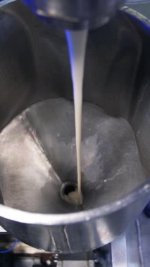 Yoğunlaştırılmış süt tüpten metal bir kaba akıyor. Kapatın. Yiyecek fabrikası otomatikleştirildi. Yukarıdan bak. Dikey video