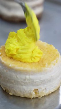 Küçük vanilyalı kek parlak sarı tereyağlı kremayla kaplıdır. Modern gıda fabrikasında tatlı dekorasyonu. Kapatın. Dikey video