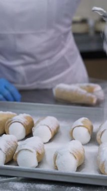 Dekorasyon için metal tepsinin üzerine tuzlu cannoli tatlısı konmuştu. İşçi tatlıları süzgeçten şeker tozuyla kaplıyor. Kapatın. Dikey video