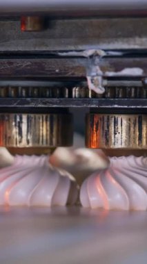 Dönen metal başlıklar, güzel şekilli şekerlemeler yaratmak için taşıyıcı bandın üzerine kremsi bir madde bırakırlar. Kapatın. Yiyecek fabrikası konsepti. Dikey video