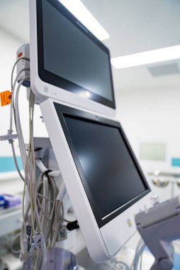 Hastane odasında tıbbi monitörler var. Hastane odasındaki ayarlanabilir bir kola monte edilmiş siyah ekranlı iki tıbbi monitör..