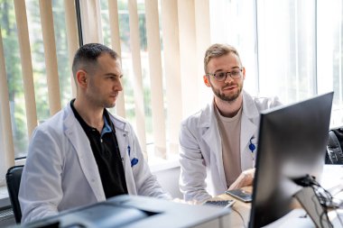 Bilgisayar üzerinde çalışan iki doktor. İki doktor bir masada oturuyor, bir bilgisayar üzerinde çalışıyorlar..
