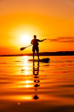 Gün batımı Paddleboard silueti. Gün batımında gölün üzerinde bir insan, parlak turuncu gökyüzüne karşı siluet.