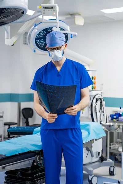 stock image Surgeon Reviewing X-Ray In Operating Room. A surgeon in scrubs and a mask reviews an x-ray while standing in an operating room.