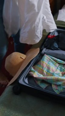 Otelde üzerinde giysiler olan bir bavul. Bavulları açan mutlu kadın. Neşeli kız giysilerini çıkarıyor ve tatilde mutlu bir şekilde dans ediyor. Dikey video