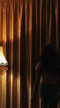 Mutlu iyimser genç bayan pencereyi açıyor. Gülümseyen kız pencereye doğru koşuyor ve lüks otel odasında karanlık perdeleri açıyor. Dikey video