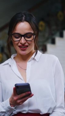 Oteldeki iş kadınının portresi. Şık gözlüklü güzel bir bayan lüks arka planda bir telefon görüşmesi yapıyor. Dikey video