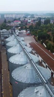 Düz sırada duran devasa metal tanklar. Demiryolları fabrika bölgesini bölüyor. Şehir manzarası ve arka planda tarım arazileri. Dikey video