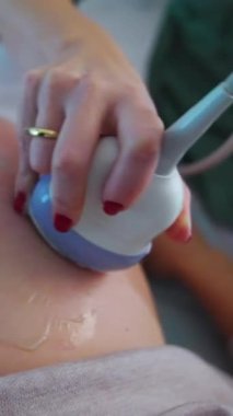 Elinde ultrasonik cihaz tutan bir doktorun eli, bir hastanın karnının üzerinde hareket eder. Kapatın. Ultrason kontrolü konsepti. Dikey video