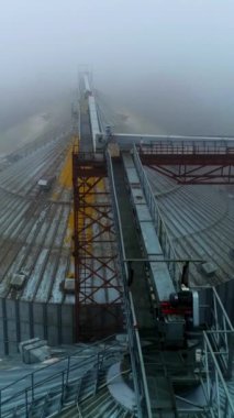 Metal ambar asansörlerinin üstünde uçuyorlar. Desteklerle birbirine bağlı dev tanklar. Sisli kış arkaplanı. Dikey video