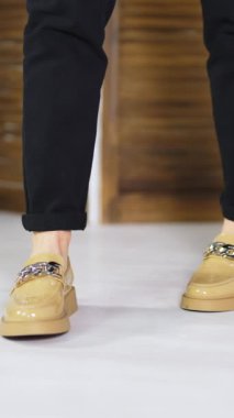 Siyah kot giyen bir kadın modelin üzerinde bej renkli rahat ayakkabılar. Gümüş zincir süslemeli yeni mokasenleri gösteriyor. Dikey video