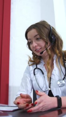 Kadın doktor bilgisayarla video konferansı yapıyor. Sıhhiye danışmanlık ve tavsiyelerde bulunuyor. İş yerindeki sevimli doktor. Dikey video