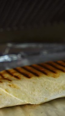 Sebzeli peynirli shawarma folyoda yatıyor. İçinde malzemeler olan ızgara pide. Kapatın. Dikey video