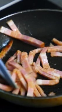 Şef kahvaltı hazırlıyor. Yağlı ve renkli harika bir domuz pastırması yapmak. Sıcak bir tavada cızırdıyor ve sigara içiyor. Dikey video