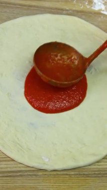 Şef kepçeyle pizza hamuruna domates sosu sürüyor. Geleneksel pizza restoranı. Yemek videosu. Yakın plan. Dikey video